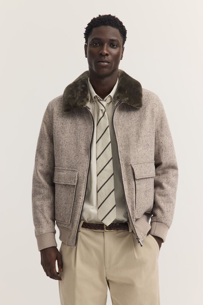 Beige speckled bomber jacket with dark olive green faux fur collar, silver-toned full-zip, two flap pockets, and ribbed cuffs