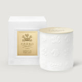 White cylindrical candle with embossed crests, horse heads, and Creed logo, topped with a gold-toned lid. White box with gold