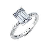 Silver-toned ring with a large clear emerald step-cut centre stone and smaller clear round stones pavé-set along the band.