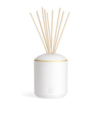White cylindrical diffuser with a rounded top, a gold-toned band, and several light wooden reeds emerging from the top.