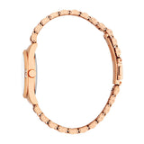 Rose-gold toned watch with a round case, fluted bezel, white dial, and three clear stones. Metal bracelet has rounded links a