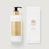White lotion bottle with black pump and gold-toned collar, next to a white embossed box, both featuring gold-toned Creed labe