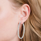 A large, silver-toned oval hoop earring with clear stones lining the outer front and inner back edges.