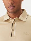 Sand polo shirt with ribbed collar and two-button placket, both featuring black and white stripes. Tonal embroidered logo on