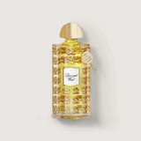 Clear perfume bottle with yellow liquid, gold-toned ornate pattern, white "Spice and Wood" label, gold-toned dome cap, and ha