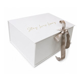 White rectangular gift box with gold-toned 'Story Loris Luxury' script on the lid, tied with a taupe satin ribbon.