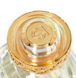 A macro, top-down view of the Touch of Oud luxury fragrance cap on Blue Salon Online. The design spotlights a polished gold center engraved with the brand emblem, enclosed in thick clear acrylic with an ornate gold filigree border.