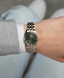 Two-toned watch with a dark green radial-textured dial, gold-toned bezel, clear stone hour markers, and a silver-toned and go